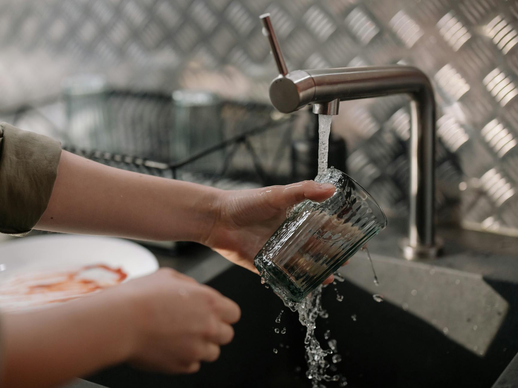 person pouring water on clear drinking glass